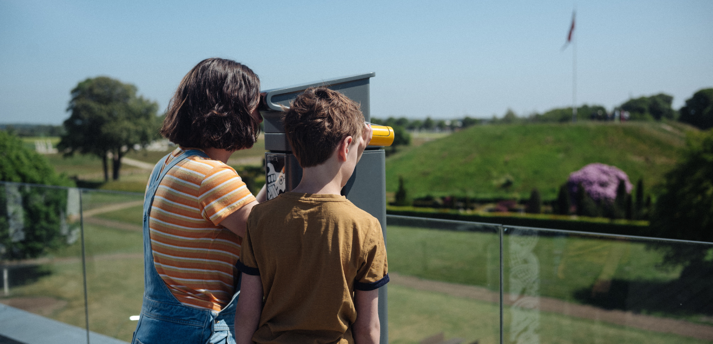 Two children look through binoculars from the roof terrace at Kongernes Jelling to the mounds