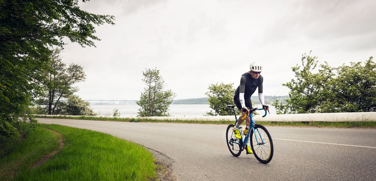 Road cyclists are heading up Munkebjergbakken. The Vejlefjord Bridge is visible in the background.