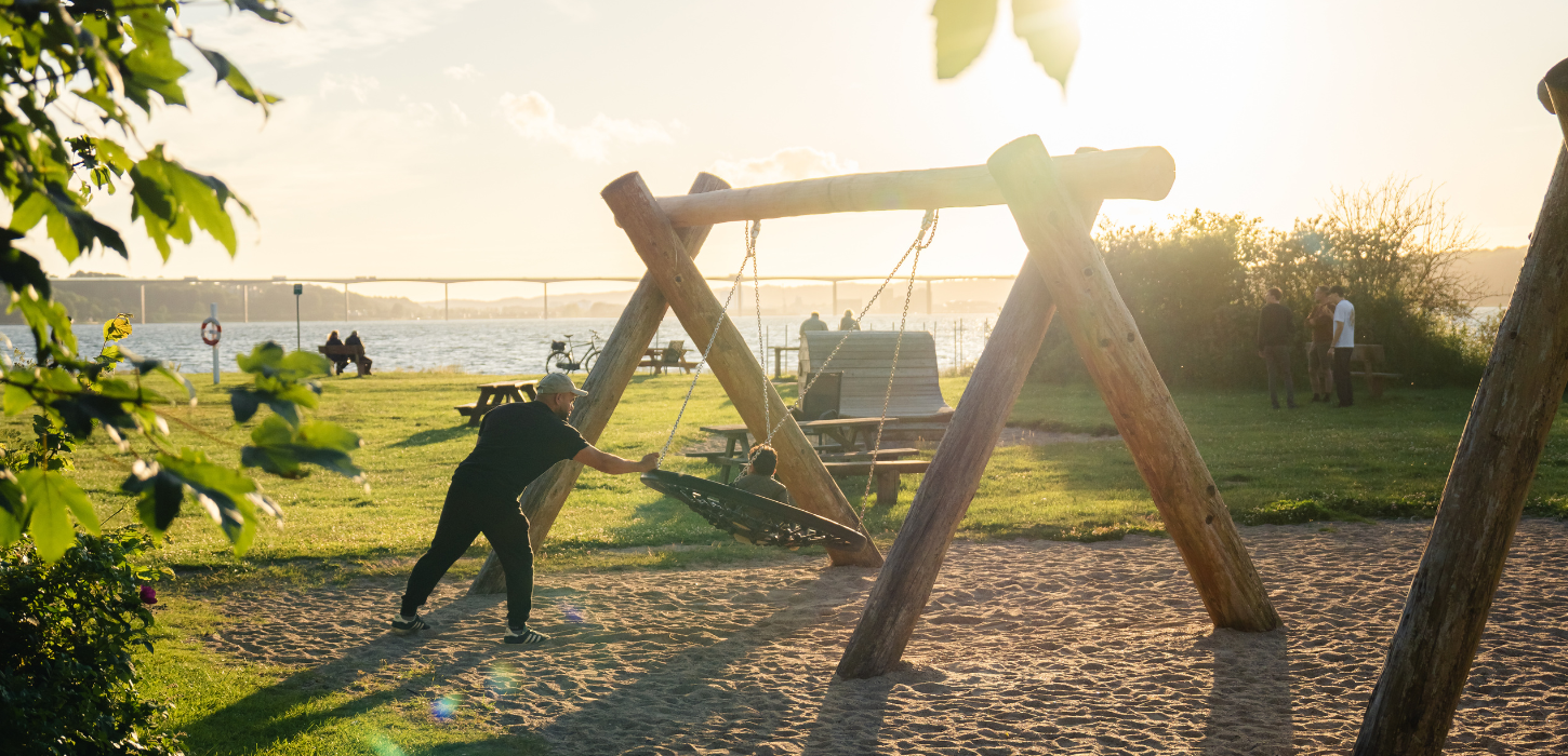 Father and child playing on a swing in the playground at Ibæk Beach