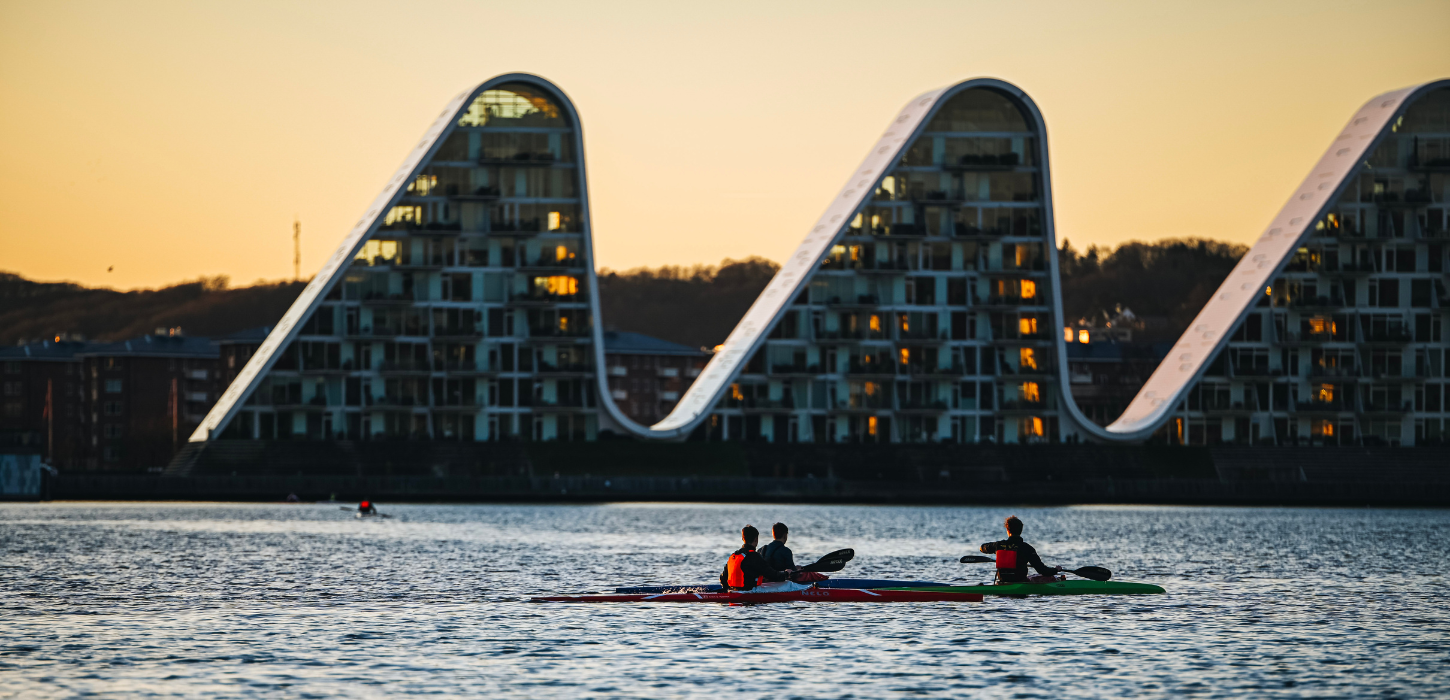 People in kayaks on Vejle Fjord with Bølgen (the Wave) in the background